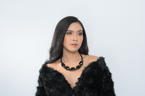 Beautiful asian model posing in a fur coat and a luxurious black gem necklace is fashion photography at studio lighting shoot on isolated gray background. Beautiful hairstyle Youth and Skin Care Concept.
