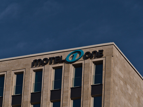 Freiburg, Baden-Wuerttemberg, Germany - 10/25/2020: Logo of budget design hotel chain Motel One (more than 70 hotels) on the top of the new constructed hotel in Freiburg center with blue sky.