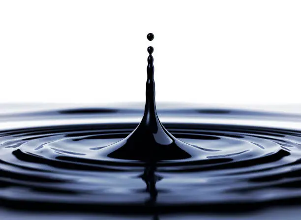 Closeup of black drop of oil or ink with ripples and white backdrop