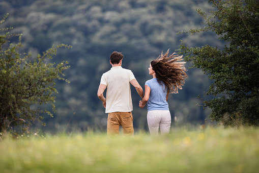 Rear view of happy couple having fun while holding hands and running in nature. Copy space.