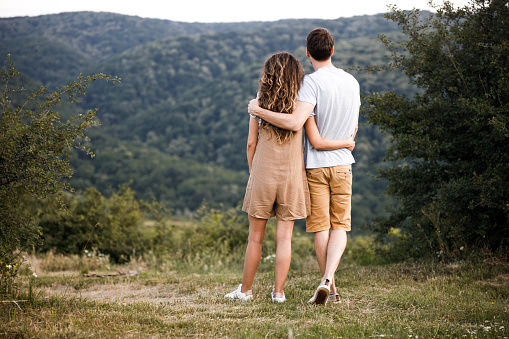 Rear view of a loving couple embracing while standing in nature and looking at view. Copy space.
