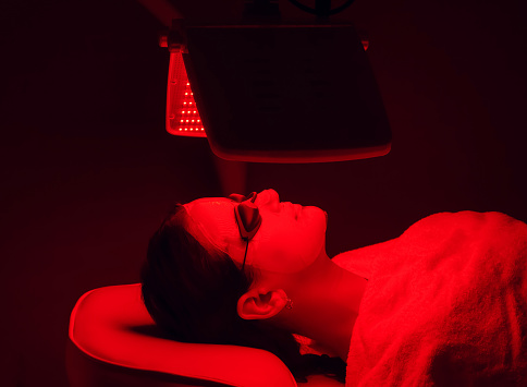 Mujer joven que tiene luz LED roja tratamiento de terapia facial en el salón de belleza. Belleza y bienestar photo