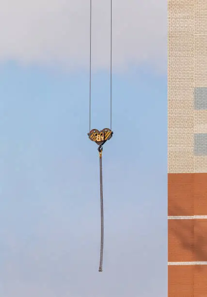 Photo of Construction site. Unfinished apartment building. Special industrial crane hook on chains in the middle. Blue sky background