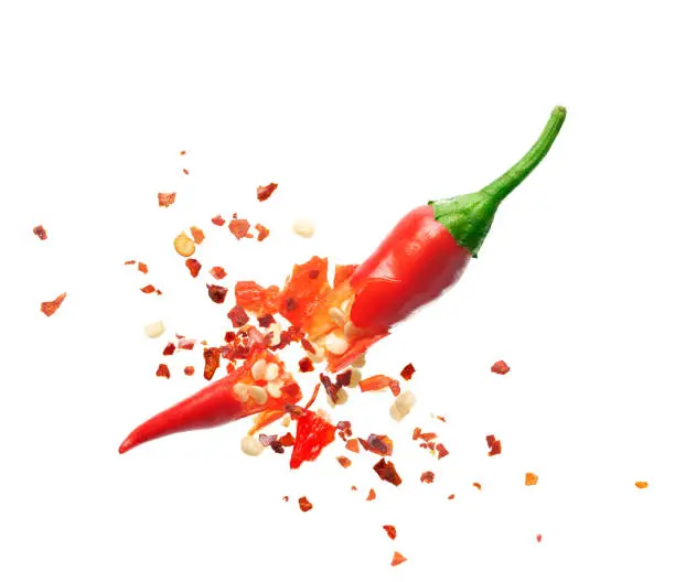 Photo of Chili flakes bursting out from red chili pepper over white background