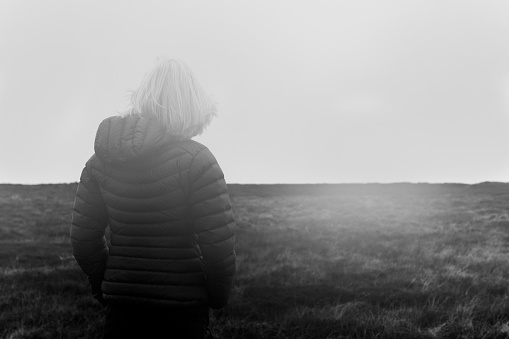 Rear view of a woman looking into the mist rendered in black and white.