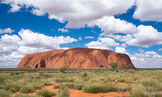Uluru, Northern Territory, Australia - March 29, 2016: Fluffy clouds drift over Uluru (also known as Ayers Rock) in the Australian Outback. A genuine Wonder of the Natural World (and a UNESCO World Heritage Site), it's also a sacred place to the local Anangu people.