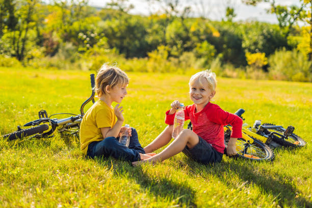 dos niños pequeños beben agua en el parque después de montar en bicicleta - 11681 fotografías e imágenes de stock