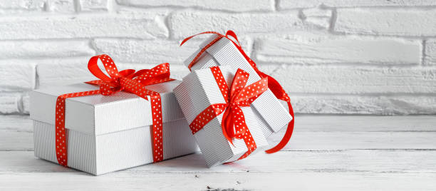 istock Set of gift boxes with red ribbon on a white wooden table, brick backdrop, banner. Selective focus. 1282992466