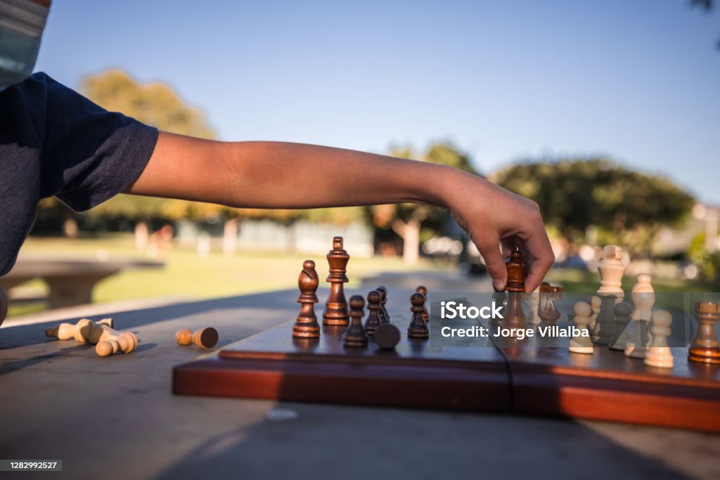 Image of boys playing at the park with a chess game and soccer while wearing a protective mask due to covid 19 Chess Stock Photo
