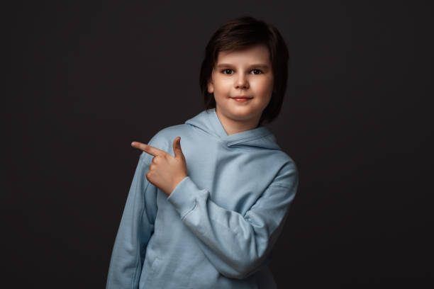 istock Cute boy shows his finger to the side, pointing copy space for your information. Studio shot, gray background 1282995160
