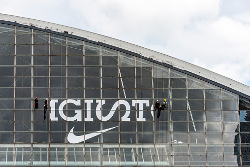 Paris, France - May 23, 2014: Facade of a corporate office building in the financial center La Defense, Paris, France. Four workers working on the windows of the office building. Nike emblem seen on the windows.