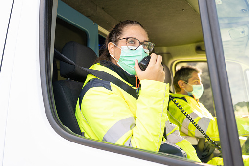 Paramedic in ambulance talking on radio with surgical mask for safety and protection during COVID-19