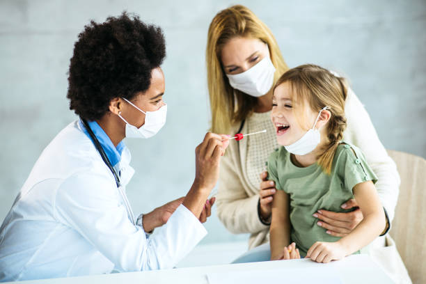 小さな女の子から喉の綿棒/pcrテストを服用している女性医師 ストックフォト
