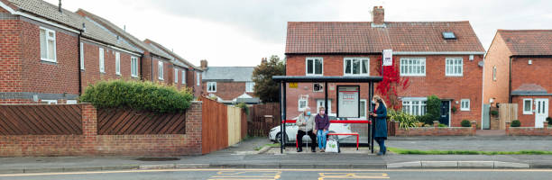 Waiting for Public Transport A wide shot of a senior, Caucasian couple and a Caucasian, mature woman waiting at a bus stop. They are all wearing a face mask to protect themselves and others from Covid-19. bus shelter stock pictures, royalty-free photos & images