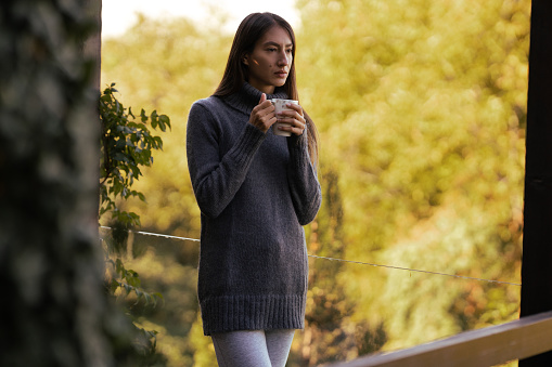 A young woman is drinking coffee and enjoying the fresh morning air on the balcony.