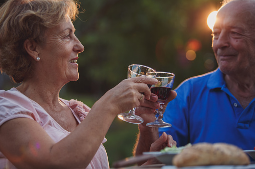 Close up of senior couple toasting with red wine during sunset to celebrate long-lasting relationship.