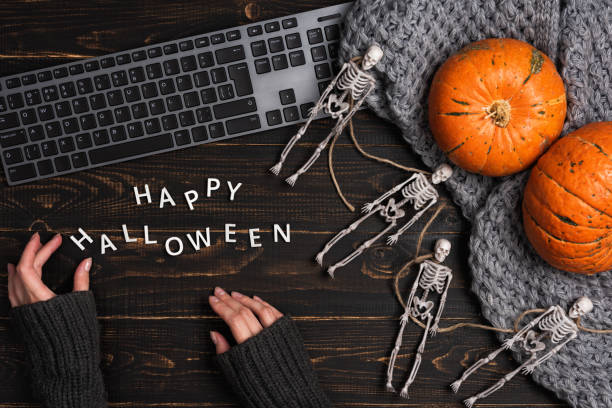 Female hands and Halloween decorations with skeleton and laptop