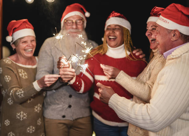 istock Cheerful senior people celebrate christmas together with sparklers firework - Elderly multiracial friends wearing christmas hats 1283012066