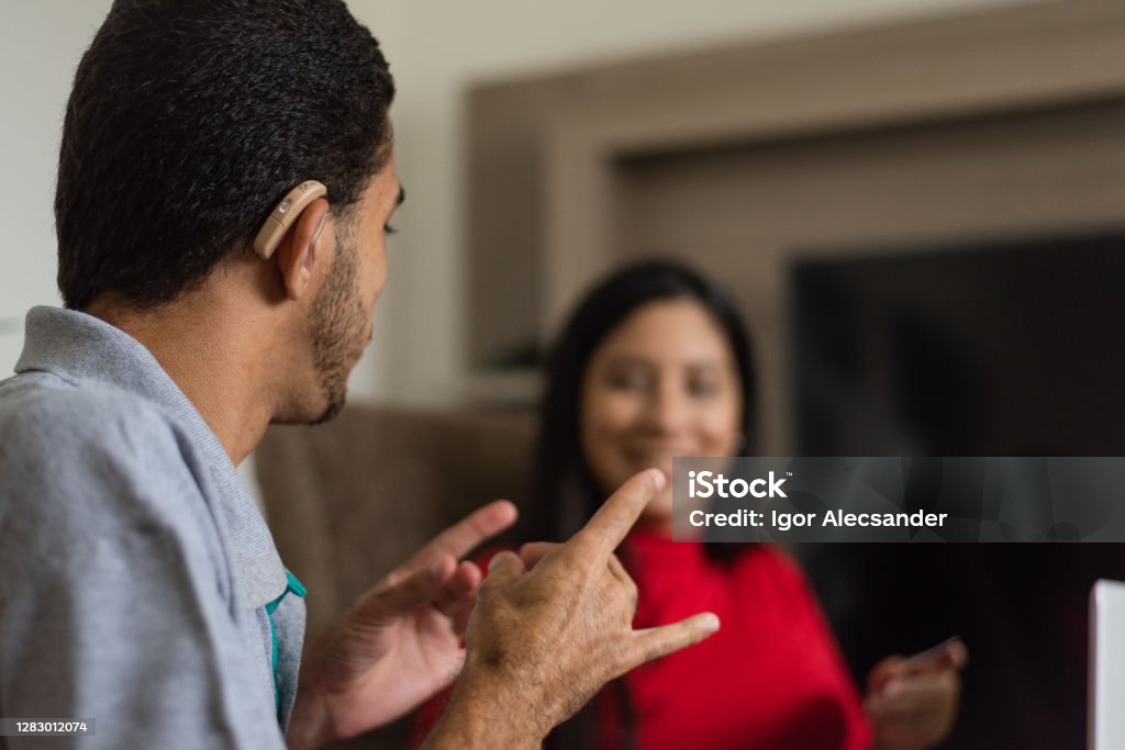 Deaf talking in sign language Deaf young people talking in sign language in the living room Sign Language Stock Photo