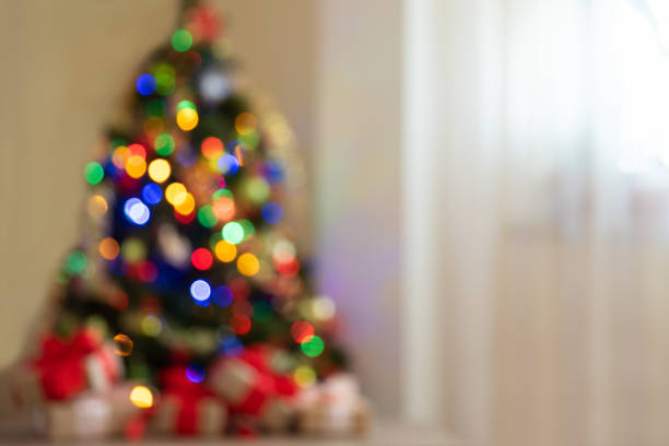istock Defocused background. Gift boxes with large red bow against Christmas tree and colorful bokeh. Copy space. Christmastime celebration concept 1283016632