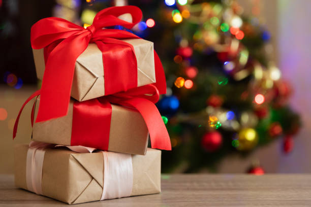 istock Gift boxes with large red bow against Christmas tree and defocused bokeh. Soft focus. Copy space. Christmastime celebration concept 1283016661