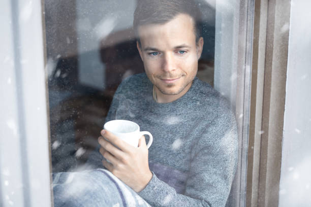 Man with a cup in his hand sitting at window during winter