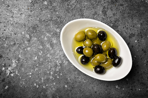 Top view of tasty mix green and black olives on grey concrete background with copy space