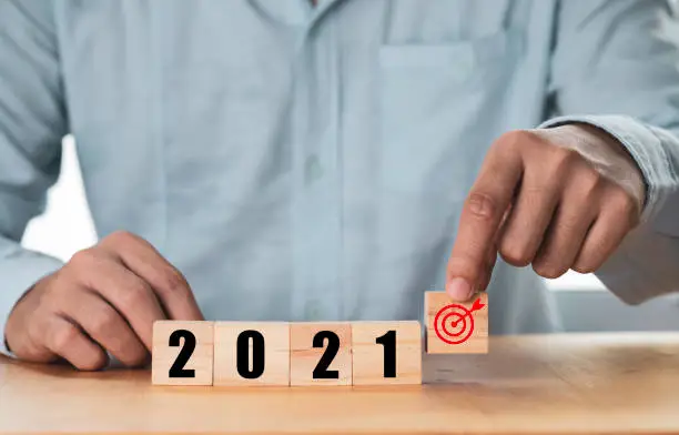 Photo of Businessman holding and putting target which print screen on wooden cube block with 2021 , Start new year and new target concept.