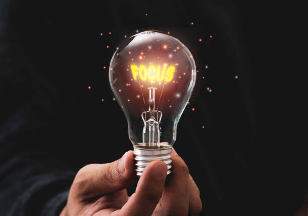 istock Focus objective target concept,Hand holding lightbulb which contain illuminating yellow focus wording. 1283020337