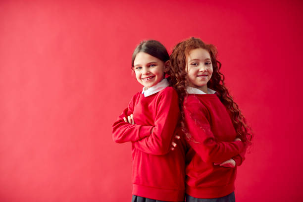 赤いスタジオの背景に背中を向けて制服を着た2人の小学生 - child 6 7 years education school ストックフォトと画像