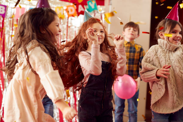 grupo de crianças dançando enquanto celebram em festa de aniversário com chapéus de papel - balloon child people color image - fotografias e filmes do acervo