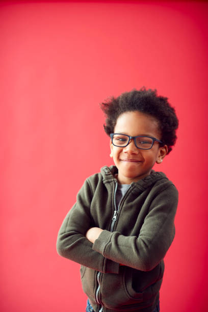 portret chłopca w okularach ze złożonymi ramionami na tle czerwonego studia uśmiechnięty do kamery - glasses child little boys happiness zdjęcia i obrazy z banku zdjęć
