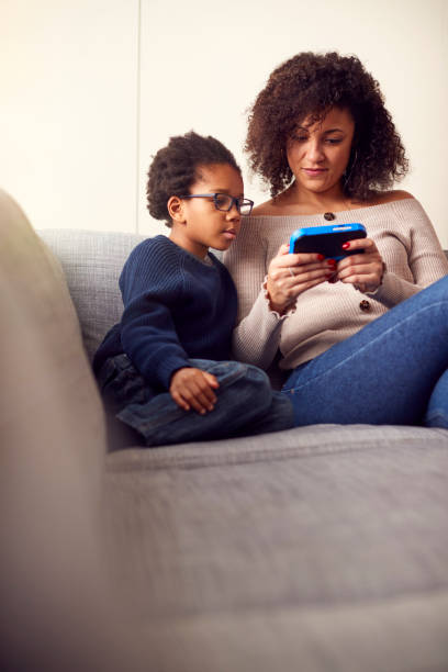 istock Mother And Son Sitting On Sofa At Home Playing Computer Game Together On Hand Held Device At Home 1283024265