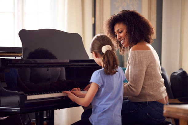 young girl learning to play piano having lesson from female teacher - music lesson imagens e fotografias de stock