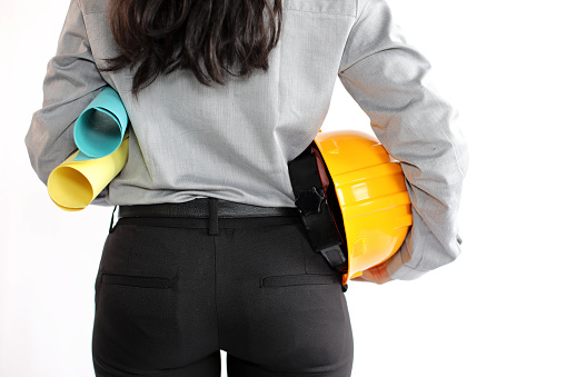 Close up of a young female civil engineer in formal wear stands holding work helmet and schematics.