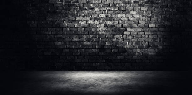 istock Studio dark room concrete floor grunge texture background with light shading on brick wall. 1283030262