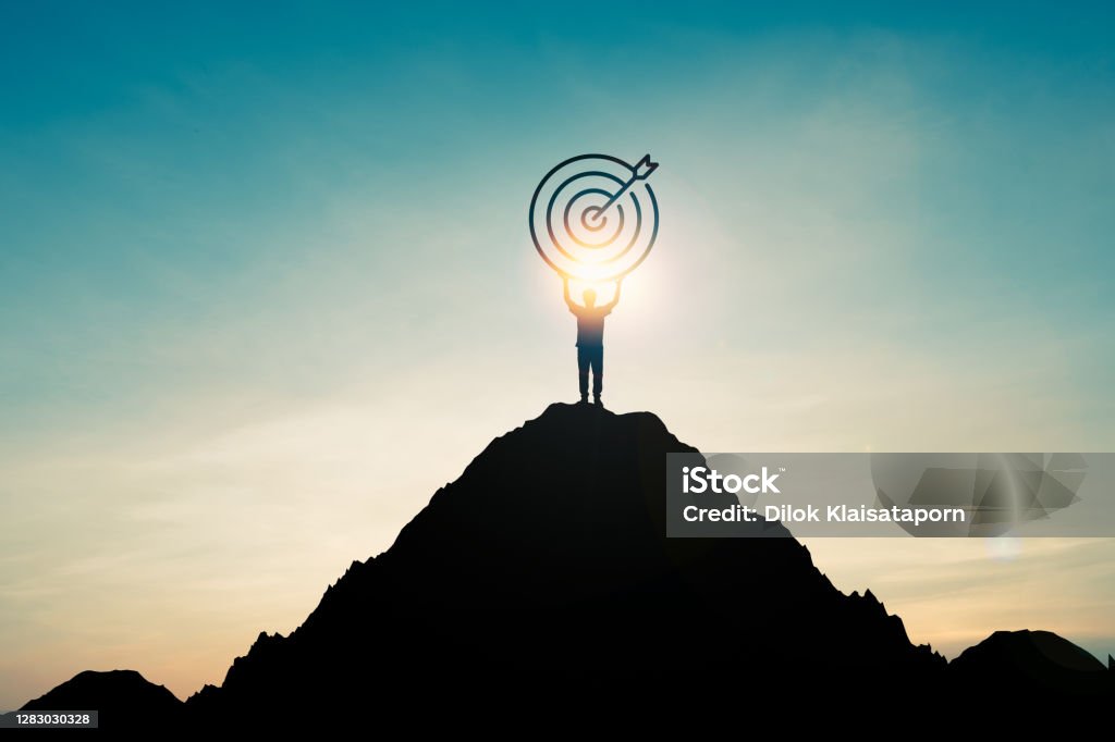 Silhouette of businessman holding target board on the top of mountain with over blue sky and sunlight. It is symbol of leadership successful achievement with goal and objective target. Aspirations Stock Photo