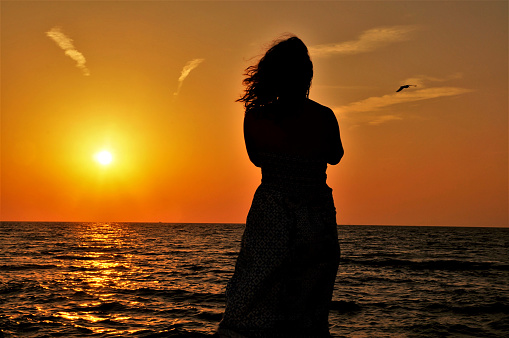 Silhouette of a young woman by the sea at sunset