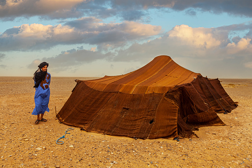 Berber people in Morocco Sahara Desert and Bedouin tent behind.