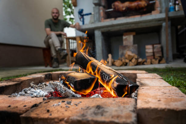 lenha queimando com homem transformando o porco "pecenje" para um evento ortodoxo na sérvia chamado slava - roasted spit roasted roast pork barbecue grill - fotografias e filmes do acervo