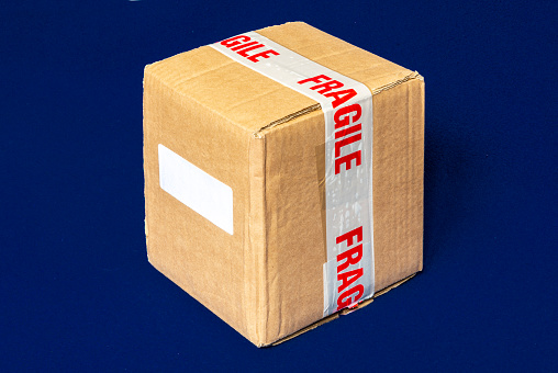 An isolated cardboard shipping box, securely wrapped with tape stating that the contents are fragile