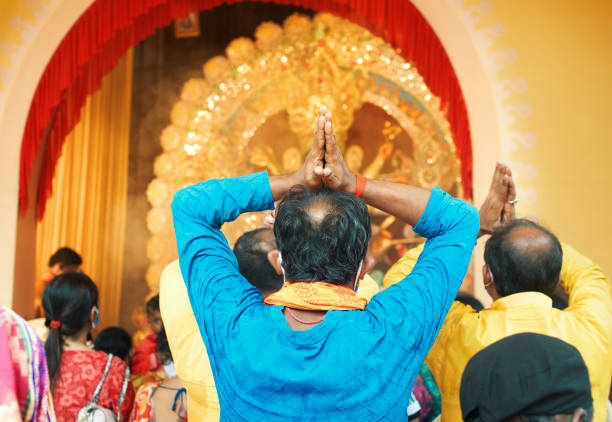 Kolkata, 10/24/2020: Among group of visitors present inside a Durga puja pandal during 'aarti' (worship), a Hindu devotee in ethnic dress is praying to idol of Goddess Durga.