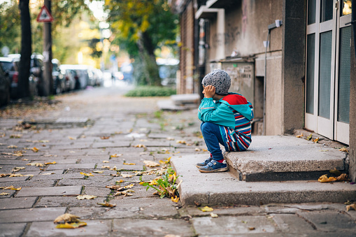 Little boy sitting alone and sad on the street