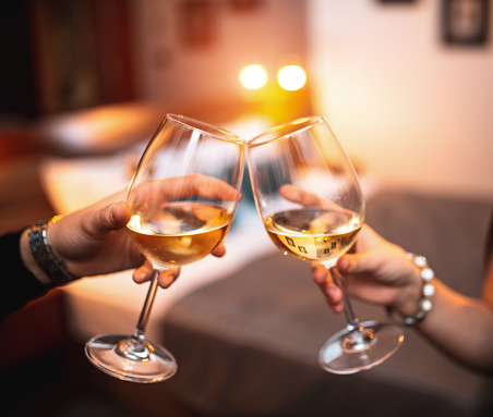 Close up of young couple toasting with glasses of white wine in hotel room