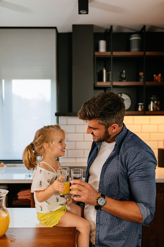 An adorable little girl and her father drinking juice together at home