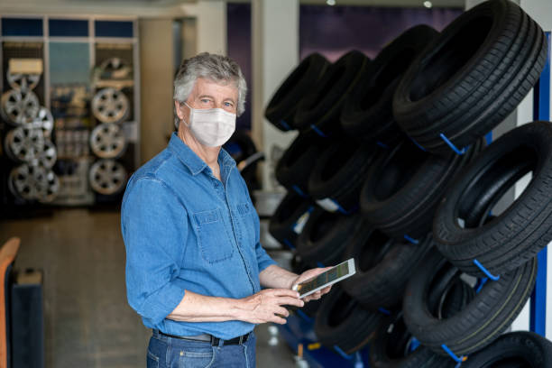 Business man working at an auto repair shop wearing a facemask selling tires Portrait of a business man working at an auto repair shop wearing a facemask selling tires during the COVID-19 pandemic auto repair shop mechanic digital tablet customer stock pictures, royalty-free photos & images