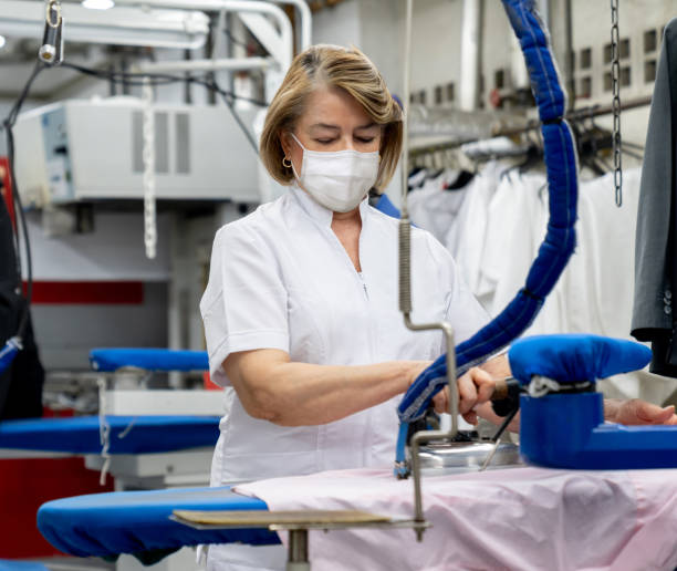 istock Woman working at a laundromat wearing facemasks and ironing clothes 1283048944