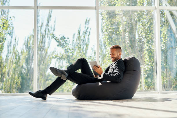 istock Smiling successful businessman in elegant suite using tablet sitting on bean bag chair 1283051130