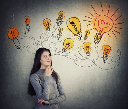 Creative young woman thinking of great ideas, looking at bright lightbulb sketches on the wall. Smart and ingenious student girl different thinking, genius solutions concept. Dream of alternative plan
