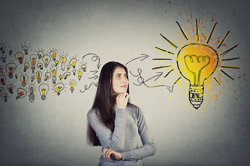 Thoughtful student girl, keeps hand under chin, looking up positive thinking for a solution. Ingenious young woman teenager gathering new ideas into a big lightbulb. Genius creativity concept.